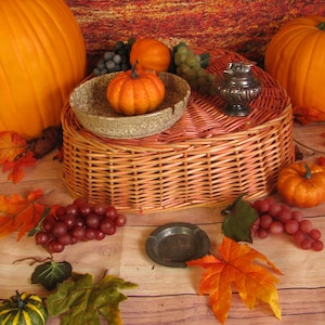 May include: A heart-shaped wicker basket with a lid, decorated with fall-themed items, including pumpkins, grapes, and fall leaves. The basket is a natural brown color with a pink stain.