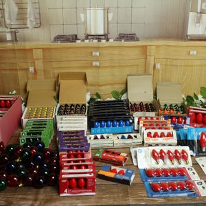 May include: A large collection of assorted replacement light bulbs for holiday decorations, including loose red, green, and blue bulbs alongside various multi-packs in cardboard boxes and plastic blister packaging, all arranged on a wooden surface.