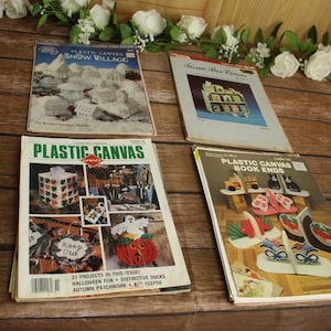 May include: Four instructional craft booklets featuring plastic canvas projects. Titles include Plastic Canvas Snow Village, Tissue Box Covers, Plastic Canvas, and Plastic Canvas Book Ends. The covers display various finished items like houses, pumpkins, and bookends.