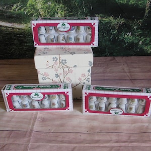 May include: Three boxes of thimbles with floral designs. The boxes are red, white, and green with the words "Thimble Collection" and "Home Styles" printed on them. The thimbles are white with floral designs.