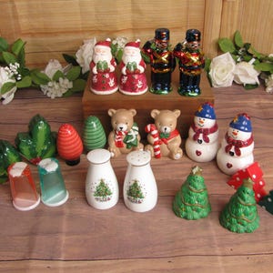 May include: A collection of Christmas themed salt and pepper shakers.  There are two Santa Claus shakers, two nutcracker shakers, two snowman shakers, two bear shakers, two Christmas tree shakers, and two green holly leaf shakers. There are also two clear salt and pepper shakers with a Christmas tree design.