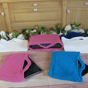 May include: Four crocheted bags in different colors, white, pink, blue, and white. The bags are made with a textured stitch and have a handle. Two of the bags are holding books, and two are holding tablets.