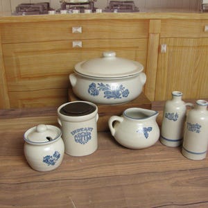 May include: A collection of off-white ceramic kitchenware with blue floral designs. Includes a lidded casserole dish, a jar labeled "Instant Coffee", a creamer, a sugar bowl, and two bottles labeled "Oil" and "Vinegar".