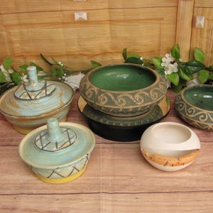 May include: Five ceramic bowls with different designs and colors. The bowls are on a wooden surface. Two of the bowls are blue and white, one is green and white, one is white, and one is green.