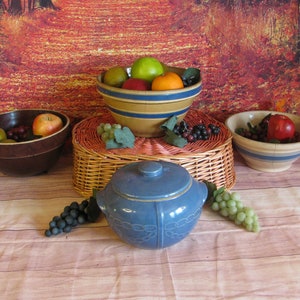 May include: Three blue and white ceramic bowls filled with fruit and grapes. The bowls are on a wooden surface with a wicker basket in the center. The background is a blurry image of a forest path.