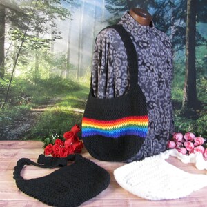 May include: Three crocheted bags, one black, one white, and one black with a rainbow stripe. The bags are all hobo style with a single strap.