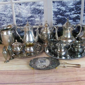 May include: A collection of silver-plated tea service items including two large coffee pots, two pitchers, two sugar bowls, two creamers, two salt and pepper shakers, two oval serving trays, and a pair of small metal tongs with a polished finish.