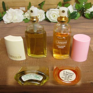 May include: An assortment of vintage perfume bottles and cologne sprays. The bottles are filled with amber-colored liquid. One bottle is labeled "L'Aimant Cologne Spray" and another "Emeraude". A pink cap and a white cap are also present.