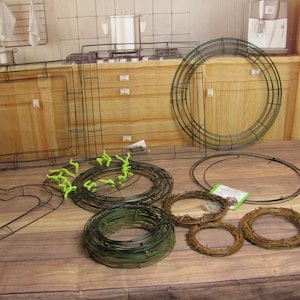 May include: Assortment of metal wreath frames in various shapes, including round, square, and heart. Several natural twig wreaths are also present. Green floral wire and other crafting supplies are visible, suggesting a DIY project.