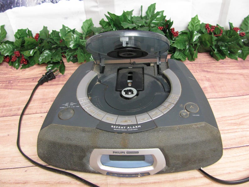 May include: A gray Philips CD clock radio with a digital display and a CD player. The CD player is open and the CD tray is visible. The radio has a repeat alarm and brightness control.