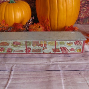 May include: Vintage metal tin box with a red and white design depicting a variety of meats and cheeses. The box is empty and has a slightly worn surface.