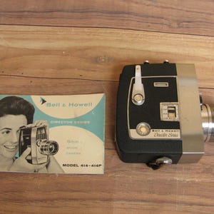 May include: Vintage Bell & Howell Director Series 8mm movie camera with a silver lens and black body. Includes a brochure with a woman holding a similar camera. Model 414-414P.