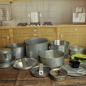 May include: A collection of miniature metal cookware including various pots, pans, lids, and a coffee percolator. The set features silver-toned aluminum items, a small black cup, a green plate, and plastic utensils arranged on a wooden surface.