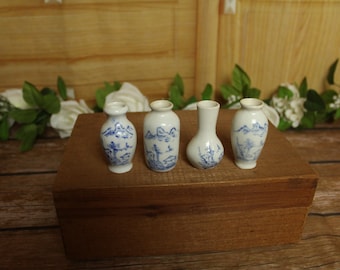 May include: Four miniature white ceramic vases with blue hand-painted landscape designs. The collection includes three vases with tapered necks and one rounded bulbous vase, all featuring detailed mountain and tree motifs in a classic blue and white style.