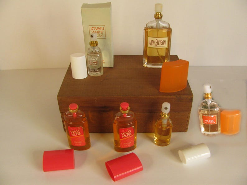 May include: Collection of vintage perfume bottles, including Jovan White Musk, Lady Stetson, and Wild Musk. The bottles are various shapes and sizes, with amber and clear glass, and red, white, and orange accents. Some bottles have their original packaging.