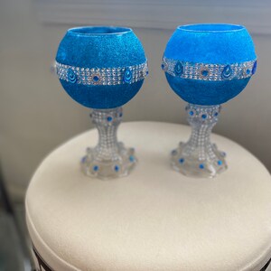 Könnte beinhalten: Zwei blaue Glaskerzenhalter mit silbernem Glitzerfinish und einem silbernen und blauen Juwelenband um die Mitte. Die Kerzenhalter stehen auf einer weißen Oberfläche.