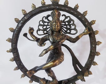 May include: A bronze statue of the Hindu deity Shiva in the Nataraja pose, dancing on a demon. The statue is set on a square base with intricate details. Shiva is depicted with four arms, holding a drum, a fire, a skull, and a hand gesture. He is wearing a crown and a long, flowing scarf.