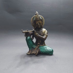 May include: A small, gold-colored statue of a Hindu deity playing a flute. The statue is sitting with its legs crossed and has a green and gold robe.