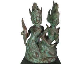 Op de afbeelding: Een bronzen beeld van twee figuren, een man en een vrouw, die samen zitten. De figuren dragen uitgebreide hoofdtooien en traditionele kleding. Het beeld staat op een zwarte houten voet.