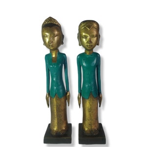 Puede incluir: Dos figuritas de madera de personas vestidas con ropa tradicional. Las figuritas están pintadas en colores dorado y verde azulado. Las figuritas están de pie sobre pequeñas bases de madera.