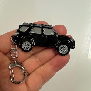Puede incluir: Llavero de metal negro con un modelo detallado de un SUV Toyota 4Runner con baca. El llavero tiene un anillo de metal plateado.