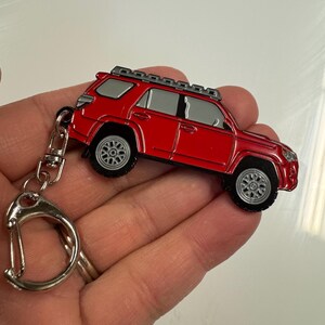 Puede incluir: Llavero de metal rojo con un modelo detallado de un SUV Toyota 4Runner con un portaequipajes en el techo. El llavero tiene un anillo de metal plateado.