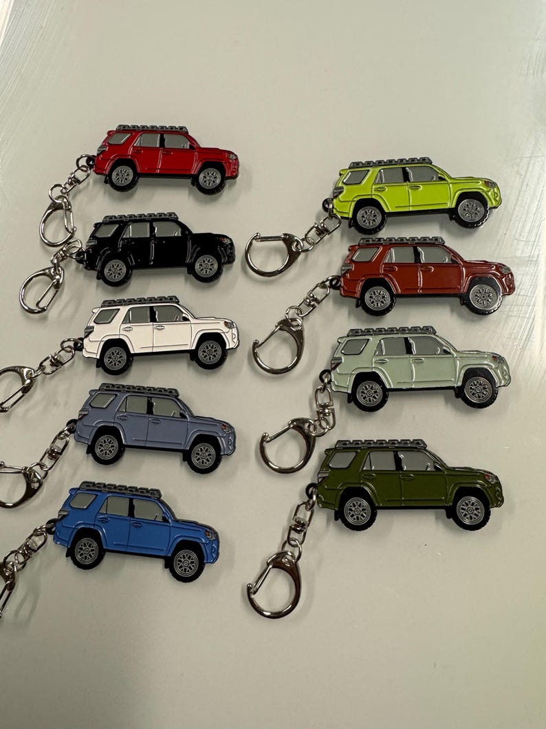 Puede incluir: Un conjunto de ocho llaveros con miniaturas de SUV de diferentes colores. Los SUV tienen un portaequipajes en el techo y est&aacute;n hechos de metal. Los llaveros est&aacute;n unidos a llaveros plateados.
