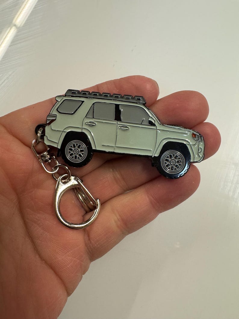 Puede incluir: Un llavero de metal verde claro con forma de Toyota 4Runner con una baca de techo negra. El llavero tiene un anillo de metal plateado.