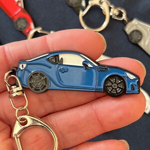 May include: A blue car keychain with a silver key ring. The car is a detailed replica of a sports car with black wheels and a white interior.