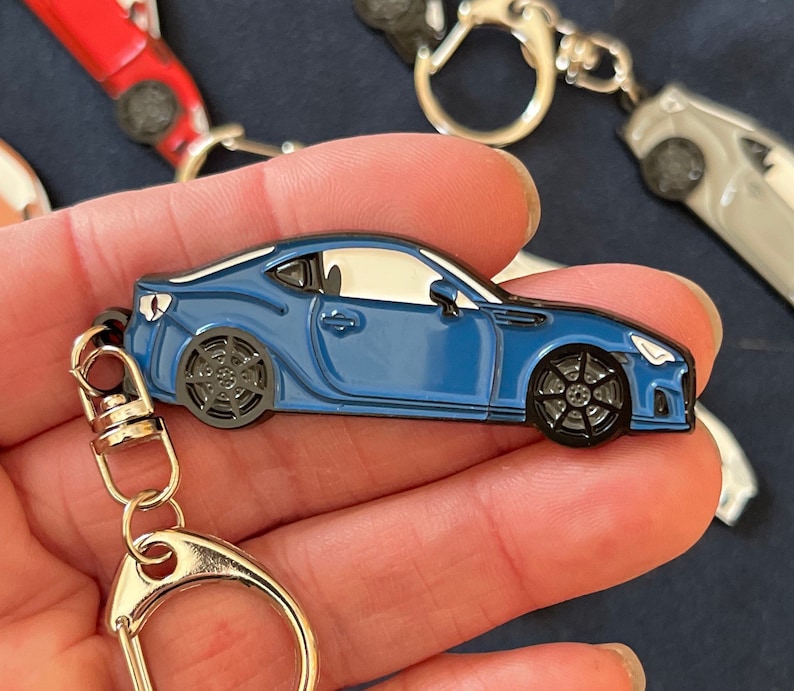 May include: A blue car keychain with a silver key ring. The car is a detailed replica of a sports car with black wheels and a white interior.