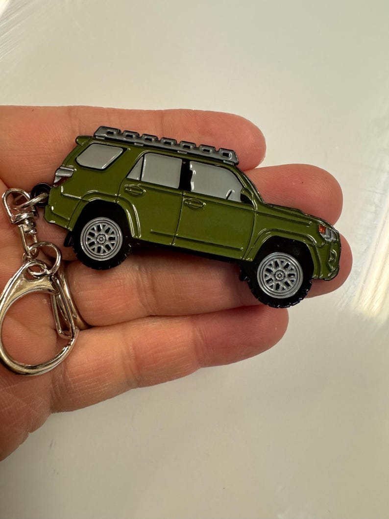 Puede incluir: Un llavero de metal verde con un modelo detallado de un Toyota 4Runner con un portaequipajes. El llavero tiene un anillo de metal plateado.