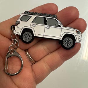 Puede incluir: Llavero de metal blanco con un modelo detallado de un SUV Toyota 4Runner con baca de techo. El llavero tiene un anillo de metal plateado.