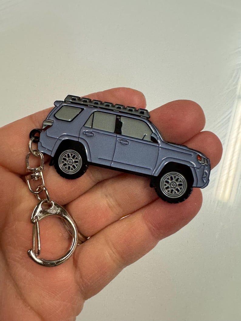 Puede incluir: Un llavero de metal plateado con un modelo detallado de un Toyota 4Runner gris con un portaequipajes en el techo. El llavero tiene un anillo de metal plateado.