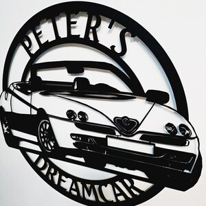 May include: Black and white metal silhouette of a car with the words "Peter's Dreamcar" around the outside.