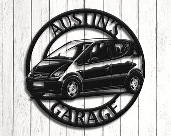Op de afbeelding: Zwart metalen garagebord met een autosilhouet in een cirkelvormige lijst. De woorden "AUSTIN'S GARAGE" zijn uit het metaal gesneden. Het bord is gemonteerd op een witte houten achtergrond, wat een contrast creëert.