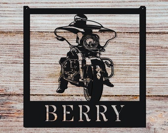 Pode incluir: Silhueta preta de metal de um motociclista com o nome "BERRY" abaixo. A imagem está sobre um fundo de madeira.