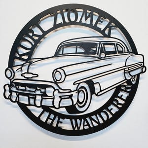 May include: Black metal cutout of a vintage car with the words "Kurt Lomek The Wanderer" around the edge.