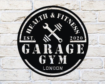 May include: Black metal sign with the words "Health & Fitness Garage Gym London" in white lettering. The sign features a wrench and barbell graphic, with "Est. 2020" at the top. The sign is circular and mounted on a white brick wall.