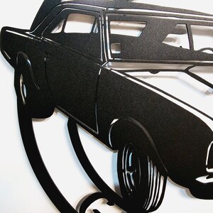 May include: Black metal silhouette of a classic car, with a detailed design of the car's body and wheels. The car is depicted in a dynamic pose, suggesting motion.