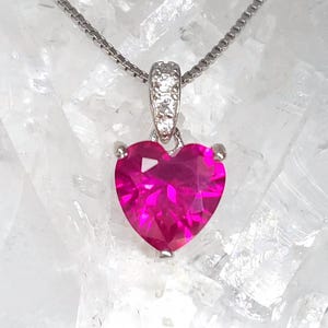 Può includere: Una collana d'argento con un ciondolo a forma di cuore in pietra preziosa rosa brillante. Il ciondolo è incastonato in una lunetta d'argento e ha una piccola cauzione scintillante. La catena è una delicata catena d'argento.