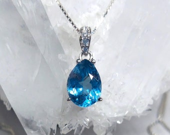 Puede incluir: Un collar de cadena de plata con un colgante de topacio azul en forma de lágrima engastado en un engaste de plata con pequeñas piedras transparentes alrededor de la parte superior.