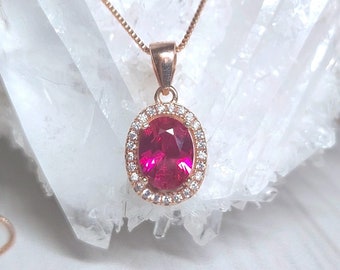 May include: A rose gold necklace with a pink oval gemstone pendant surrounded by smaller clear gemstones.