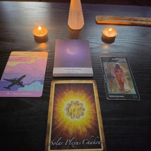 Pode incluir: Quatro cartas de tarot dispostas numa superfície escura com duas velas acesas e uma ponta de cristal translúcida. As cartas apresentam um avião com o texto Plan a Vacation, um eclipse roxo com A time for healing, uma figura e um Solar Plexus Chakra.