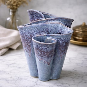 May include: A blue ceramic vase with a unique, multi-compartment design. The vase has a textured surface with a speckled pattern and a dark brown rim. The vase is a decorative item for the home.