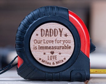 May include: A red and black tape measure with a wooden circle that says "Daddy Our Love for you is Immeasurable Love Miles & Mila".