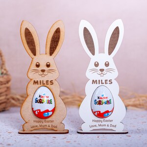 Personalised Easter Egg Holder made from 3mm wood or 4mm Beech Veneered Wood, Egg holder has a cut out to fit Kinder Surprise Egg and Cadbury Egg Creme, Name engraved in front of the wooden Easter bunny standing with a base.