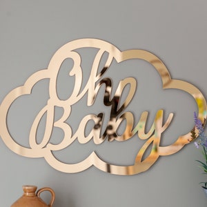 Może przedstawiać: Złoty, lustrzany znak w kształcie chmury z napisem "Oh Baby" w ozdobnym, pisanym stylu.