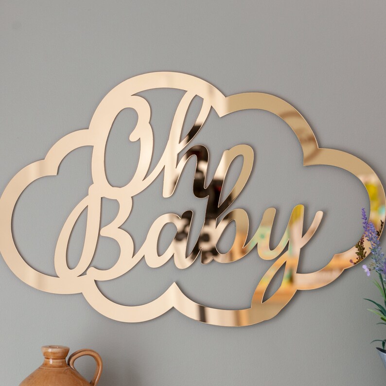 Może przedstawiać: Złoty, lustrzany znak w kształcie chmury z napisem "Oh Baby" w ozdobnym, pisanym stylu.