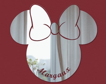 Könnte beinhalten: Ein silberner Spiegel in Form von Mickey Mouse Kopf mit einer weißen Schleife. Der Spiegel trägt den Namen "Margaux".