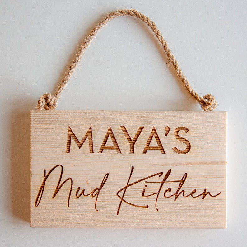 Peut inclure: Une pancarte en bois avec le texte "MAYA'S Mud Kitchen" grav&eacute; dessus. La pancarte est suspendue &agrave; une corde.